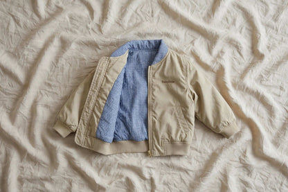 Veste bomber réversible enfant Varenne beige avec doublure à carreaux bleus sur fond texturé.